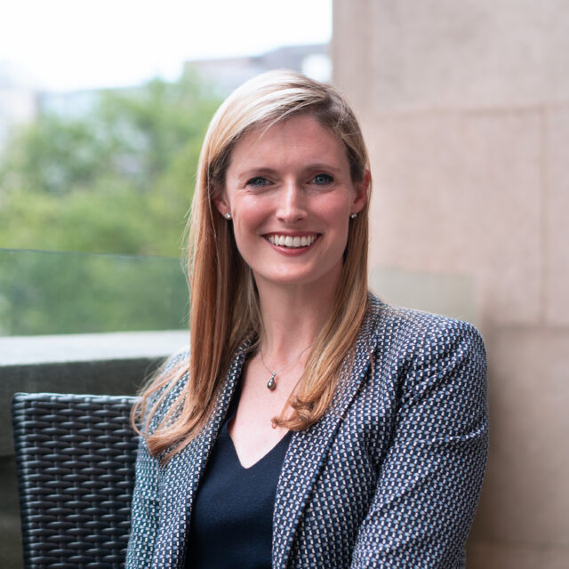 CDT President & CEO Alexandra Reeve Givens. Wearing a patterned jacket and blue dress, seated outdoors.