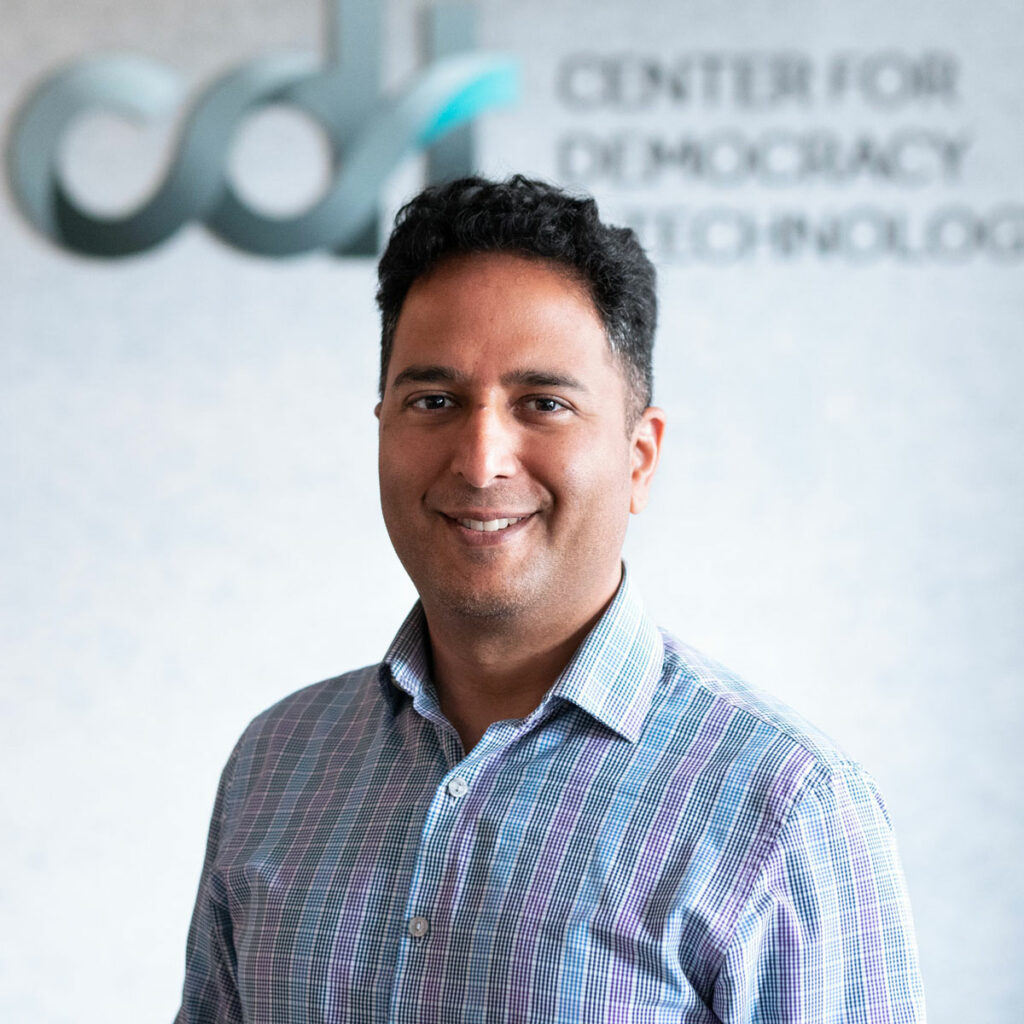Dhanaraj Thakur, in a blue striped collared shirt smiling in front of the CDT logo.