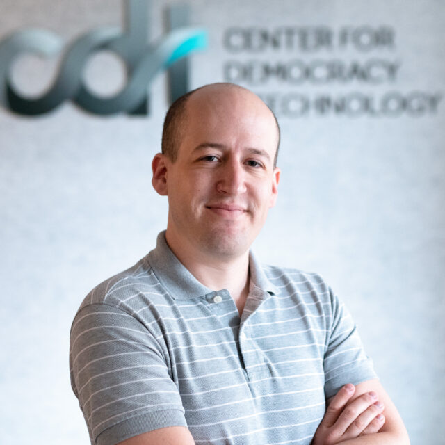 Will Adler, crossing his arms and smiling in a grey striped polo, in front of the CDT logo.
