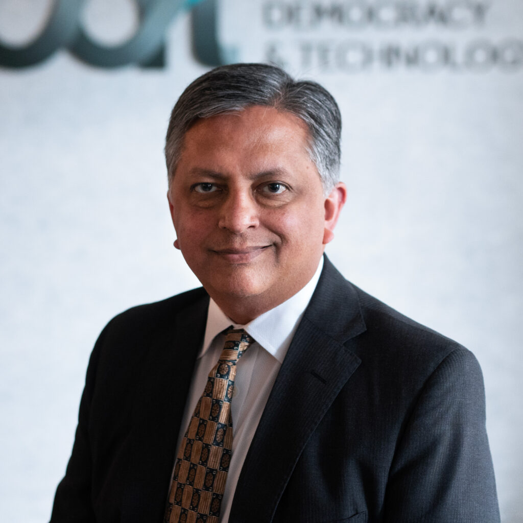 Samir Jain, smiling and wearing a dark suit, white collared shirt and patterned tie in front of a CDT logo.