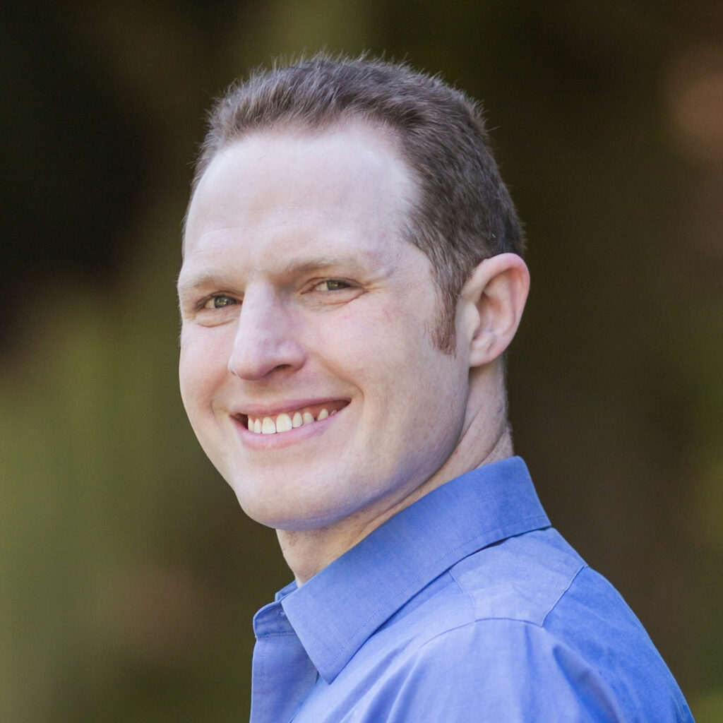 Matthew Scherer, smiling outdoors wearing a blue collared shirt.