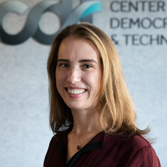 CDT's Caitlin Vogus, wearing a red top and a red stone necklace, in front of the CDT logo in the background.