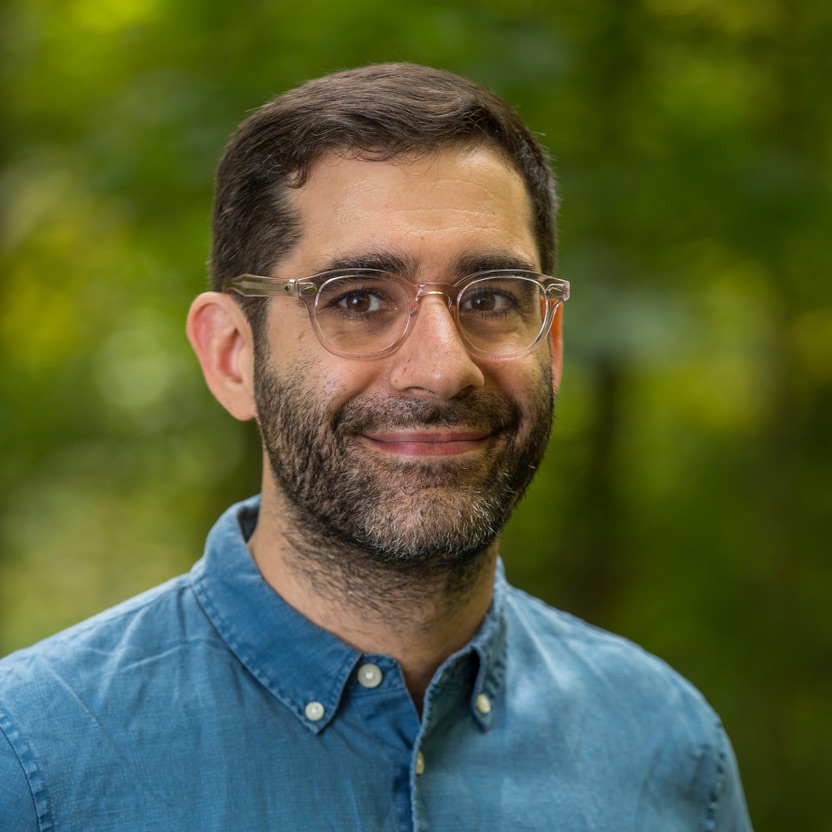 Image of Solon Barocas, wearing glasses and a collared shirt in front of a green background.