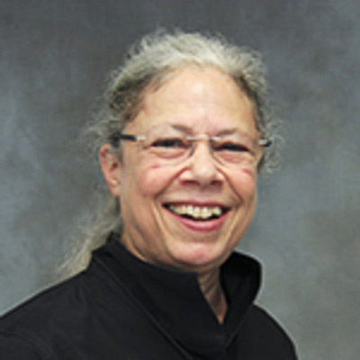 Sandra Braman. Abbott Professor of Liberal Arts, Texas A&M. Wearing glasses and a black sweater, in front of a grey backdrop.
