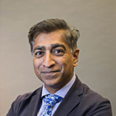 Anupam Chander. Professor of Law, Georgetown Law. Grey suit with a blue shirt and tie.