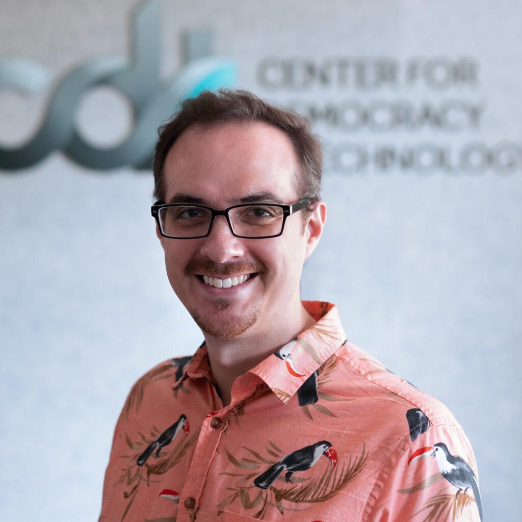 Eric Null, wearing dark rimmed glasses and a pink toucan collared shirt, in front of a CDT logo.