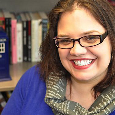 Casey Fiesler. Assistant Professor, University of Colorado. Wearing glasses and a scarf, in front of a bookcase.