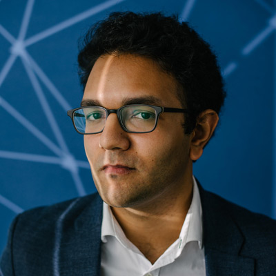 Dipayan Ghosh. Fellow, Platform Accountability Project, Harvard Kennedy School. Wearing glasses and a dark suit with white collared shirt, in front of a blue prism background.
