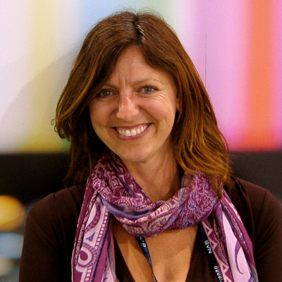 Jennifer Holt. Professor, University of California at Santa Barbara. Wearing a black shirt and a purple scarf, in front of a multi-color background.