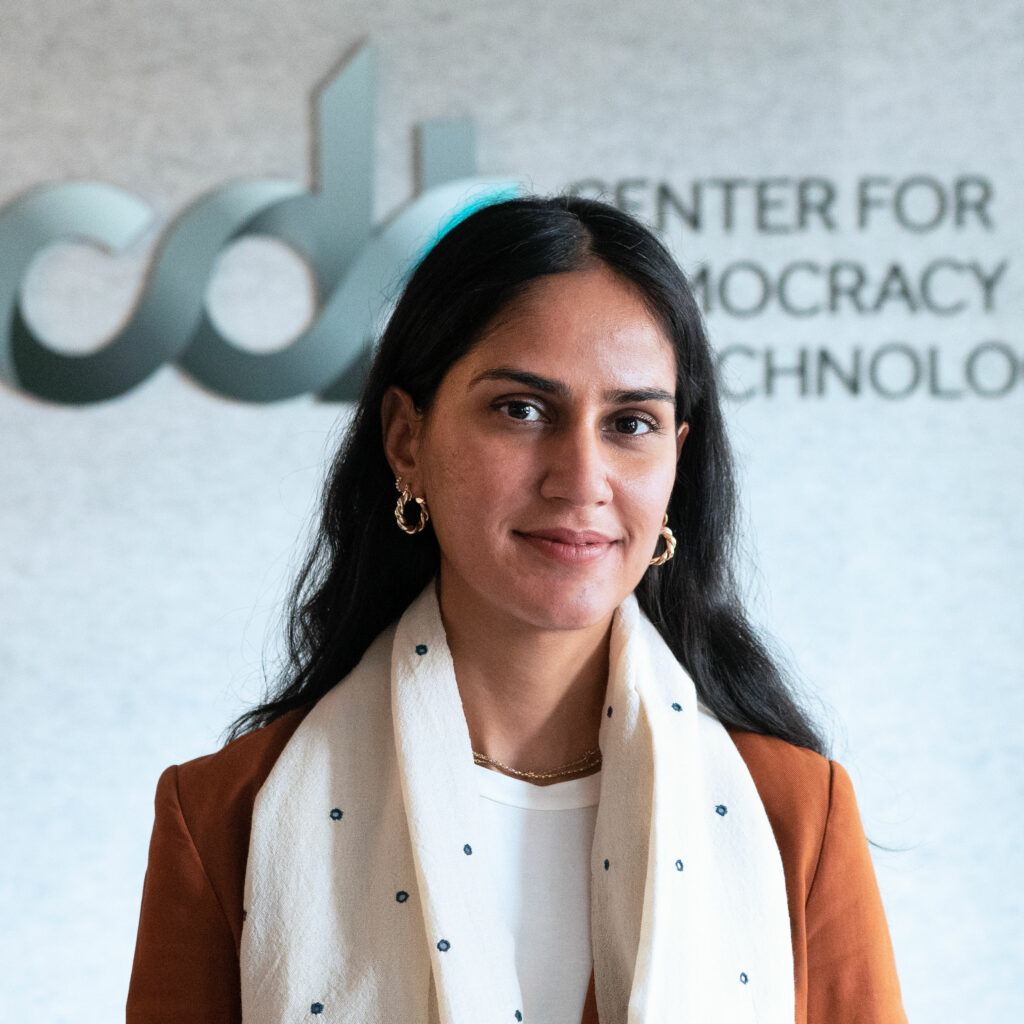 Aliya Bhatia. Wearing a brown jacket and white patterned scarf in front of a CDT logo.