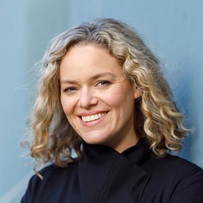 Katherine Maher. Wikimedia Foundation. Wearing a black shirt in front of a light blue background.