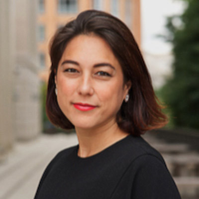 Laura Moy. Georgetown University. Wearing a black shirt in front of a building and leafy green background.