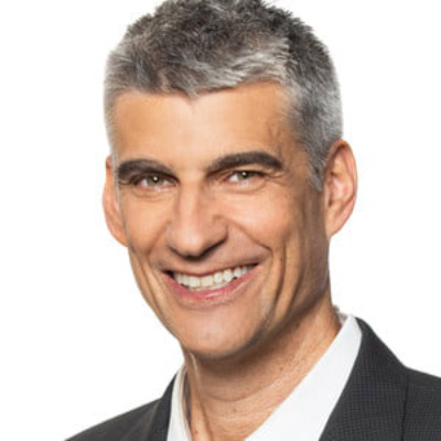 Michael Petricone. Consumer Technology Association. Wearing a white collared shirt and a dark grey suit, in front of a white backdrop.