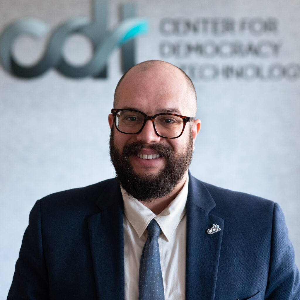 Jake Laperruque, wearing a blue suit and blue tie, and brown glasses in front of the CDT logo.