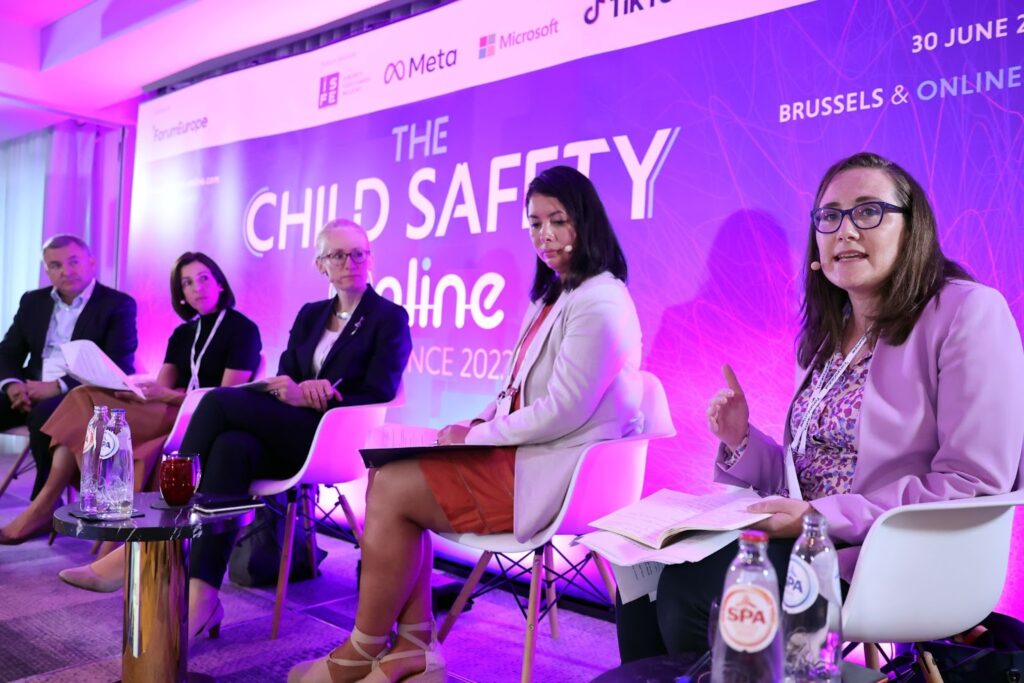 CDT Europe's Iverna McGowan, seated on stage at Forum Europe’s Child Safety Conference, wearing a light purple jacket and glasses while speaking alongside other panelists. 