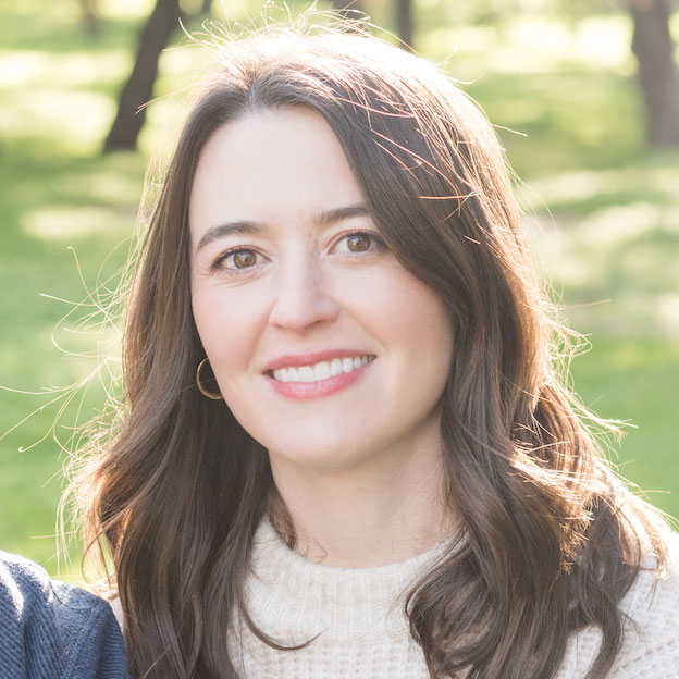 CDT Fellow Caitlin Burke, wearing a tan sweater and washed in sunlight outdoors in front of a green background.