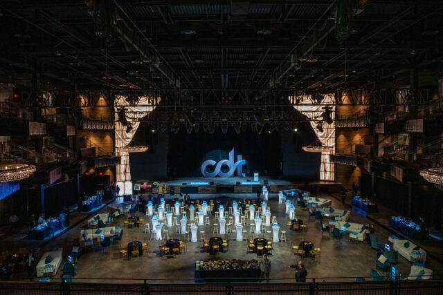 The Anthem's main stage, dressed for CDT's 2022 Tech Prom. Large "CDT" logo spotlighted on stage, while the room is filled with lounges, tables, and chairs.