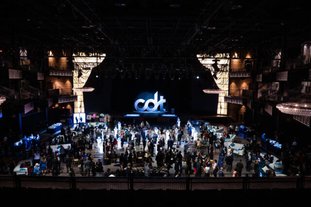 The Anthem's main stage, dressed for CDT's 2022 Tech Prom. Large "CDT" logo spotlighted on stage, while the room is filled with people chatting across lounges, tables, and chairs.