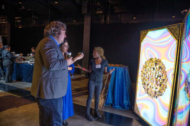 Guests look at and discuss an AI art installation while holding drinks at CDT's 2022 Tech Prom.