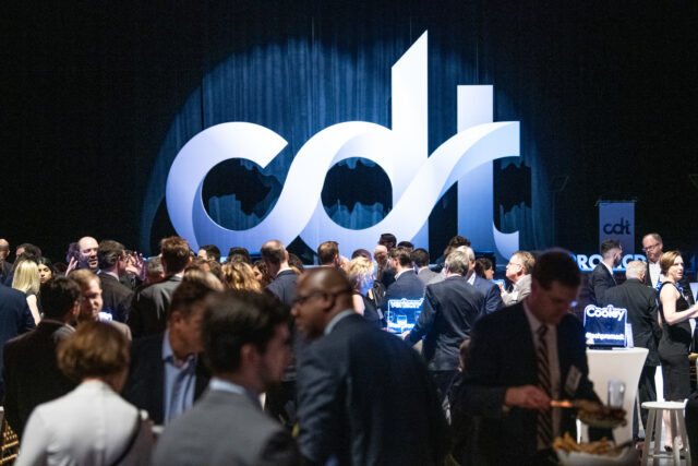 Guests at CDT's 2022 Tech Prom mix and mingle, with a large CDT logo in spotlight on stage.