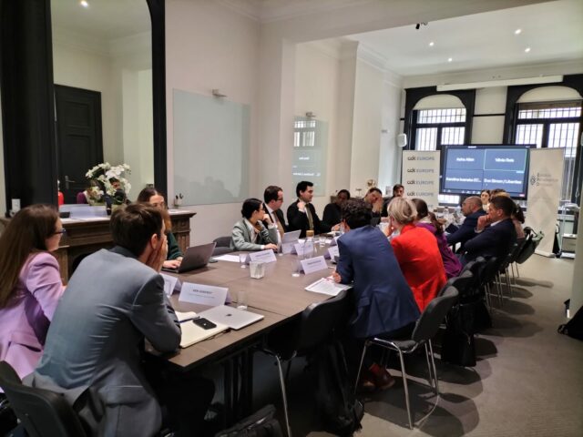 Photograph of 18 participants seated at an U-shaped table. A screen is transmitting the video conference. Iverna McGowan, Director of CDT Europe, sits at the front of the table, with representatives from different Member States on the right side of the room. On the left side of the table, Fernando Hortal Foronda from the European Partnership of Democracy (EPD) sits next to Asha Allen, Advocacy Director for Europe and Civic Space at CDT Europe and moderator of the panel.