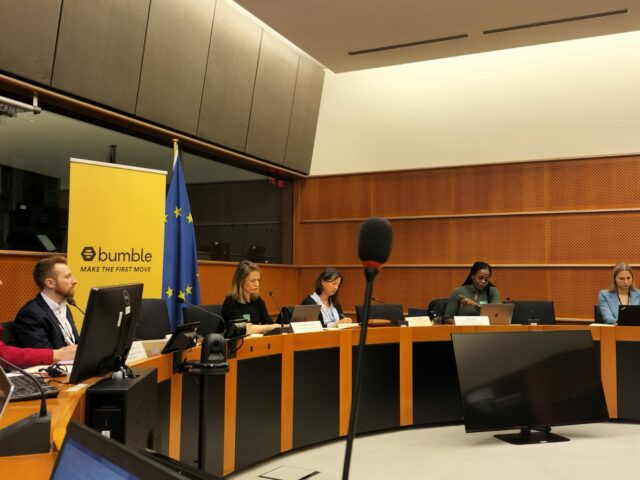 Photograph of roundtable participants, including CDT Europe's Asha Allen at second from right, sitting at a table in front of a yellow Bumble yellow banner and an EU flag.