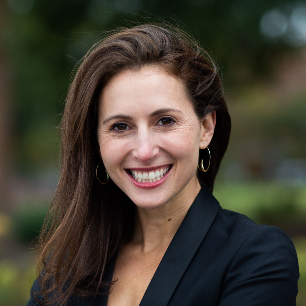 Sarabeth Berman, wearing a black jacket and smiling in a green outdoor setting.