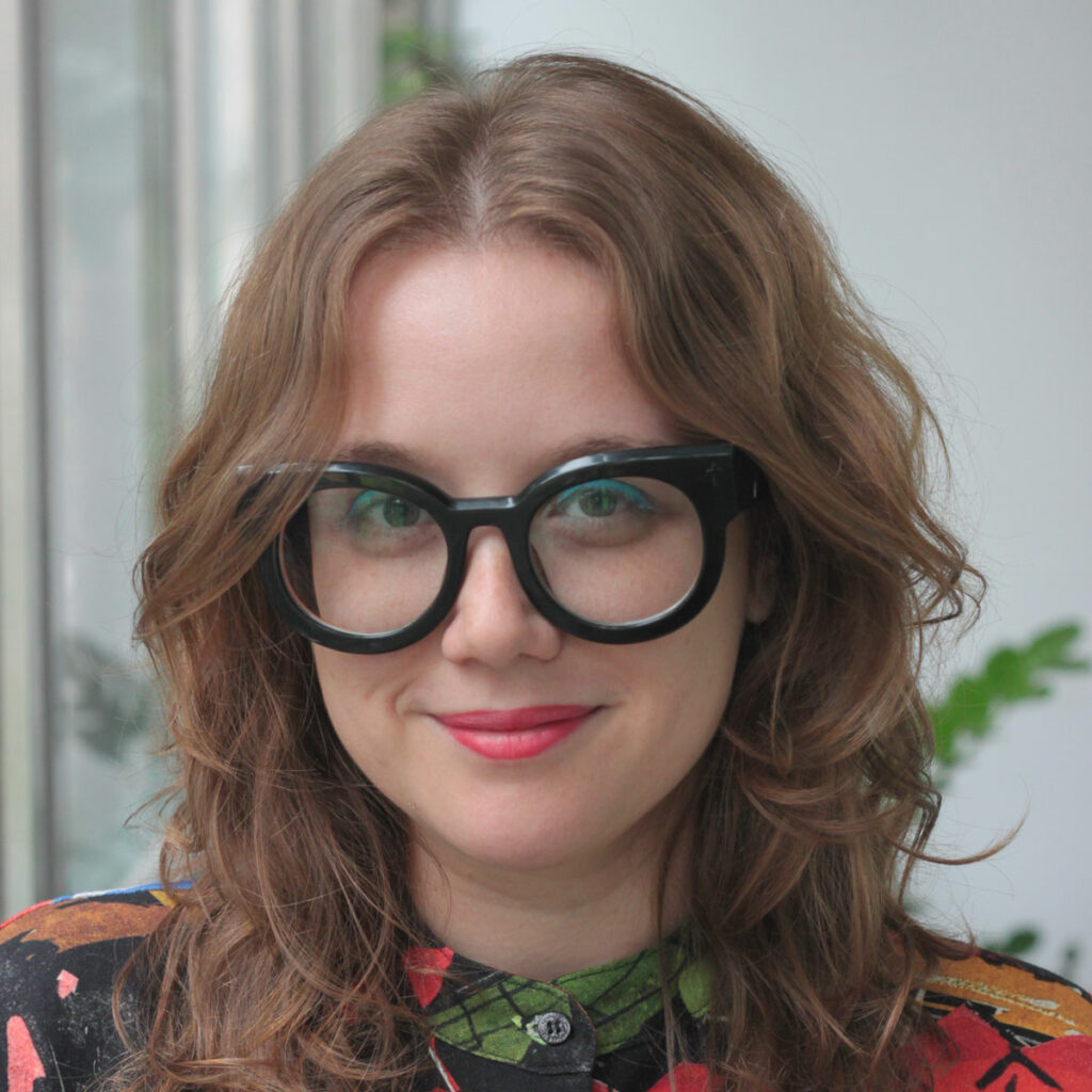 Jess Reia, wearing black glasses and a brightly patterned top.