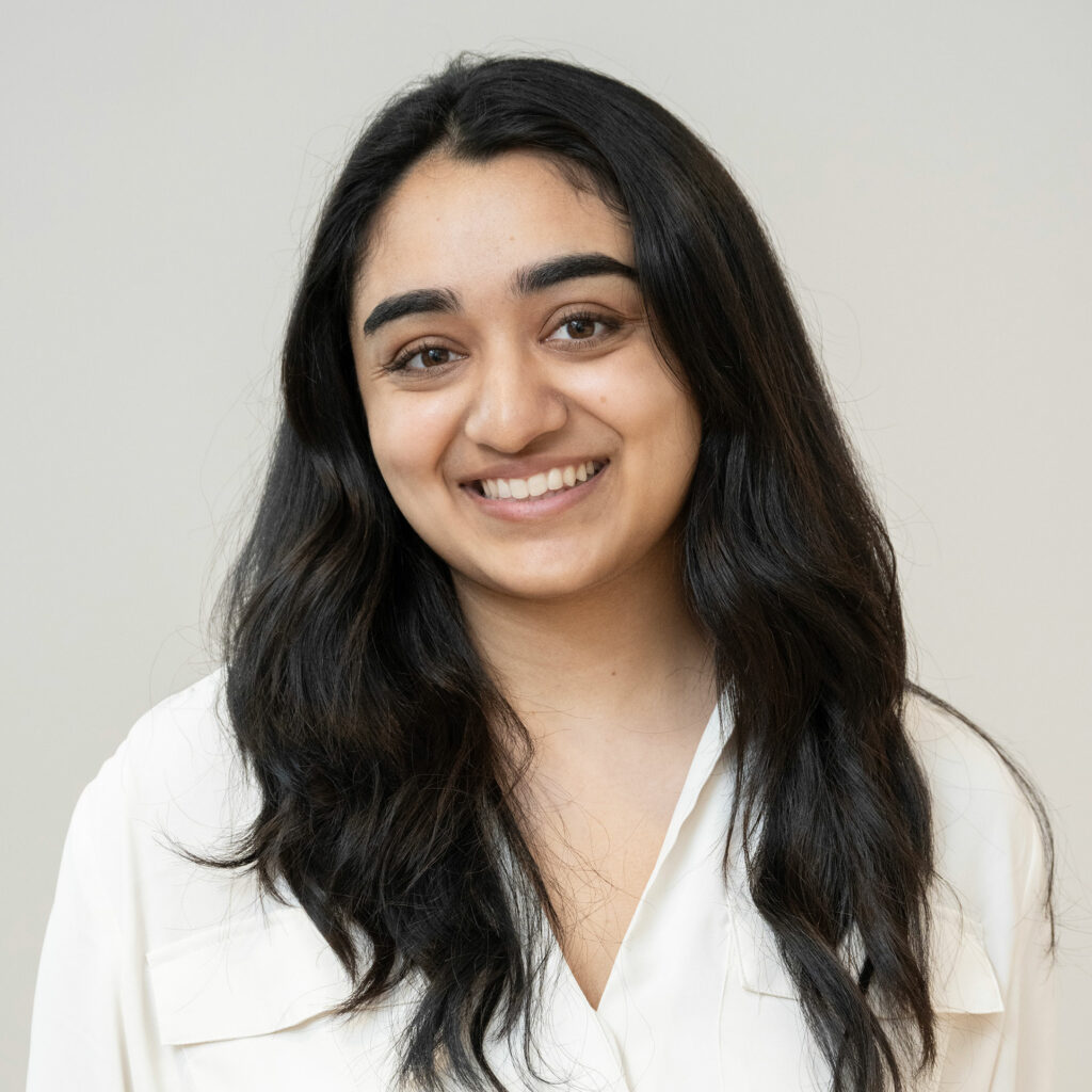Sahana Srinivasan, smiling wearing a light colored top in front of a light colored background.