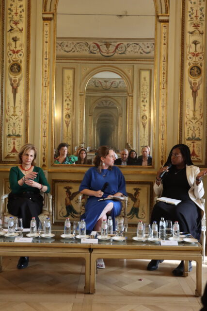 Photograph of three speakers appearing onstage, including CDT Europe’s Programme Director for Online Expression & Civic Space Asha Allen at far right of image, on a panel organised by the UK Mission and the Brussels Binder.