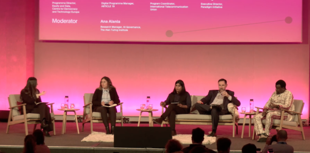Image featuring Programme Director for Equity and Data Laura Lazaro Cabrera speaking at a panel with three other panelists on the role of fundamental rights in standardisation, at the Global AI Standard Hub Summit