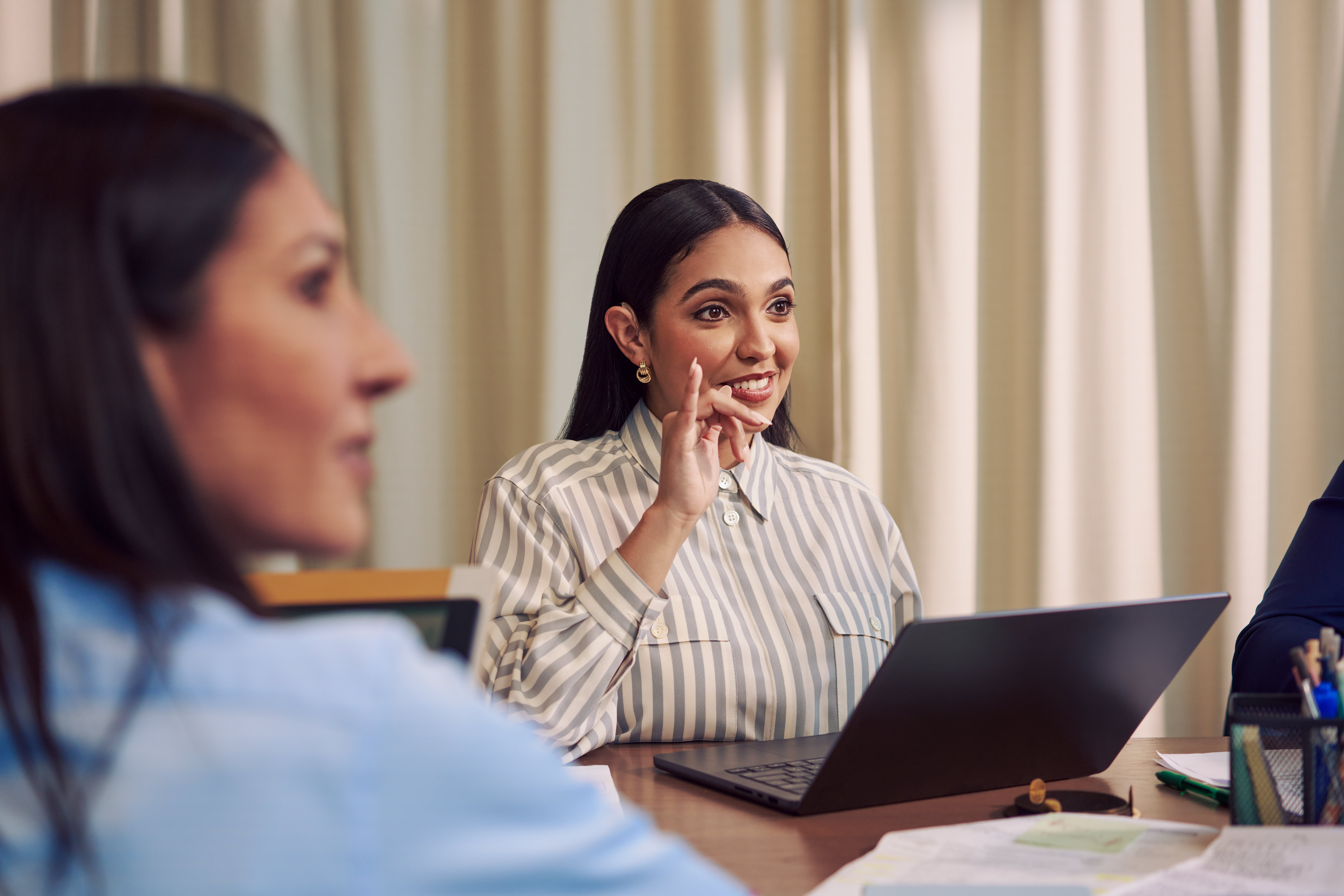 A Deaf Latina Puerto Rican woman communicates in American Sign Language to a white hard of hearing man sitting across from her at a conference room table.