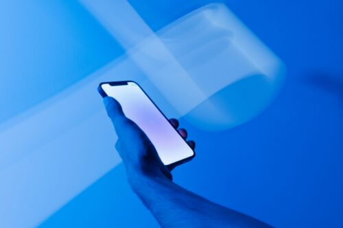 A hand holds a bright glowing phone against a deep blue, blurry background.
