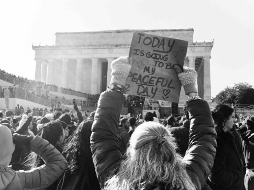 Black-and-white photo of a gathering celebrating the end of the Walk for Peace. A woman holds a sign at a protest in front of the Lincoln Memorial in Washington, D.C.