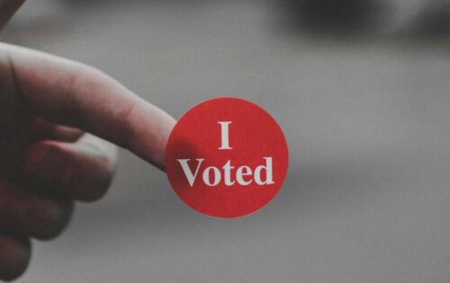 A photograph of a hand with an I Voted sticker on the index finger.