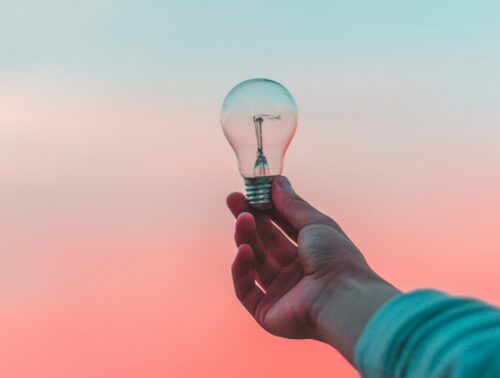 Image of a hand holding a light bulb in front of a blue and pink background.