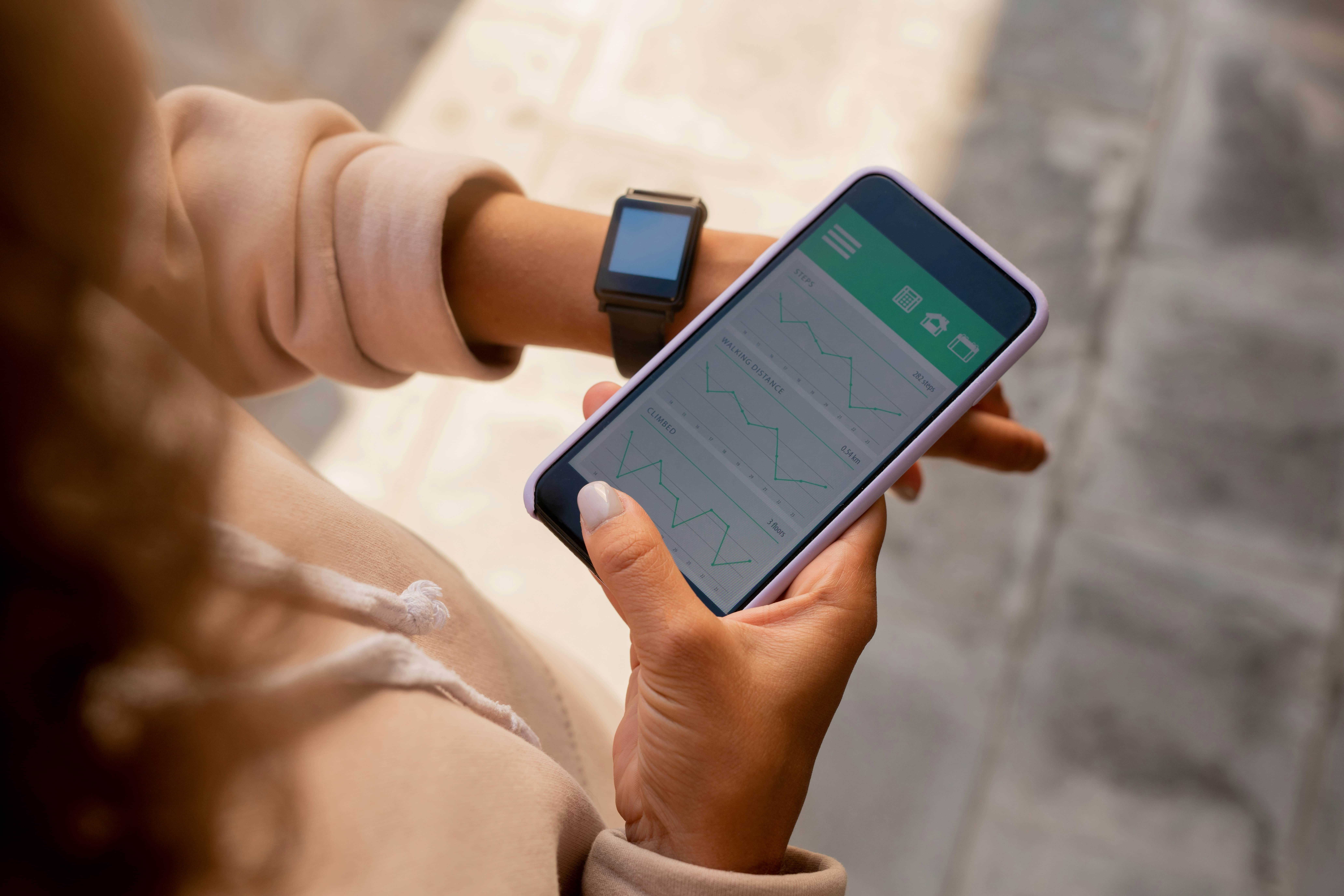 Photo of a person wearing a light colored hoodie and looking down at their phone and smart watch.