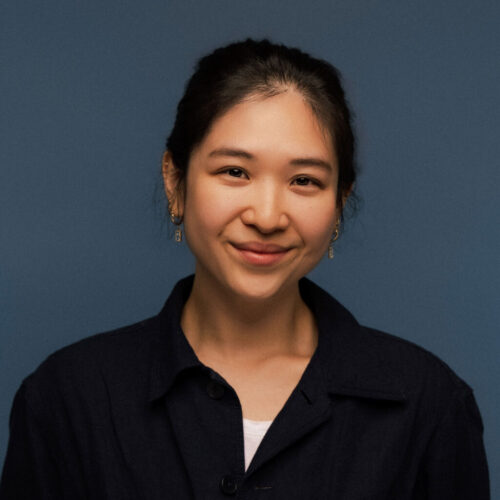 Minsoo Thigpen, smiling in a black collared shirt in front of a dark blue background.