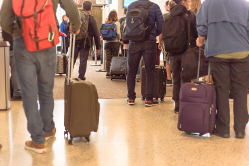 Rear view long queue of passengers waiting with carry on luggage before on boarding to airplane at Seattle, Washington, USA airport. Diverse group of multicultural travelers standing