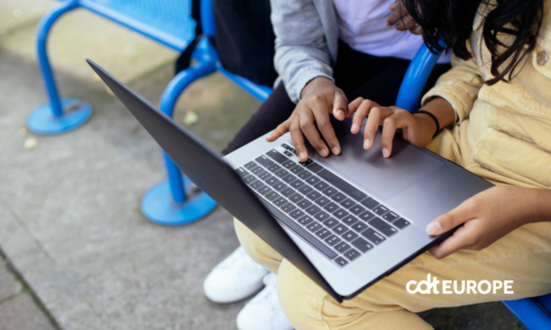 Two teenagers using a laptop together on a blue bench outdoors